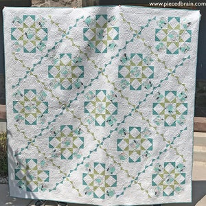 May include: A white quilt with a repeating pattern of teal and green squares and circles. The quilt is made with a variety of fabrics and has a quilted texture.