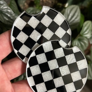 May include: Two black and white checkered round coasters with a glittery finish
