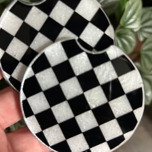 May include: Two black and white checkered round coasters with a glittery finish.