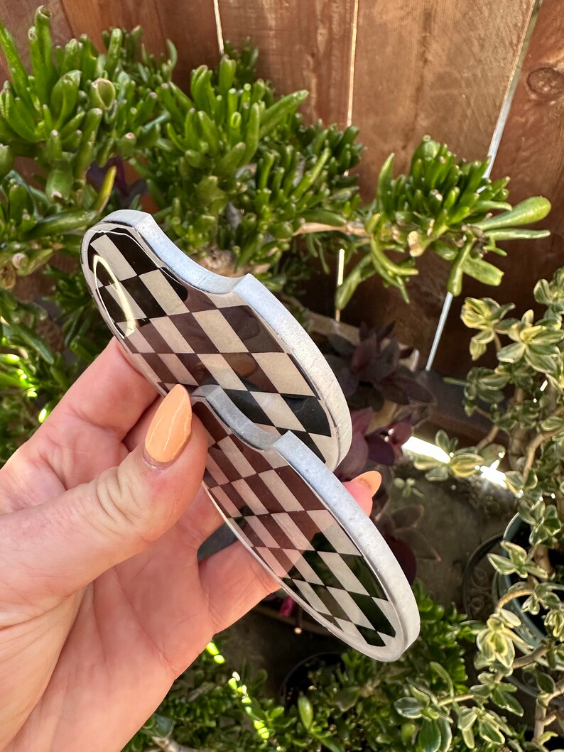 May include: Two black and white checkered coasters with a silver rim. The coasters are made of a hard, durable material and are perfect for protecting surfaces from spills and scratches.