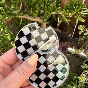 May include: Two black and white checkered round coasters with a glossy finish.