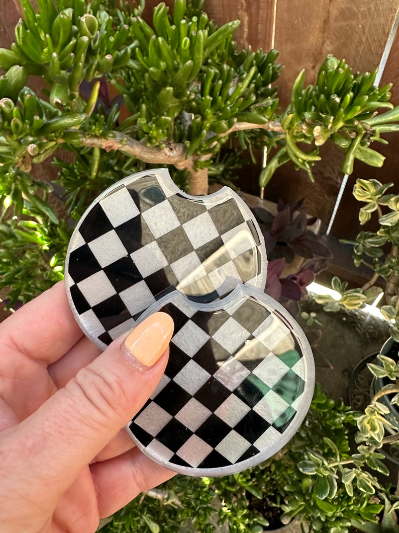 May include: Two black and white checkered round coasters with a glossy finish.