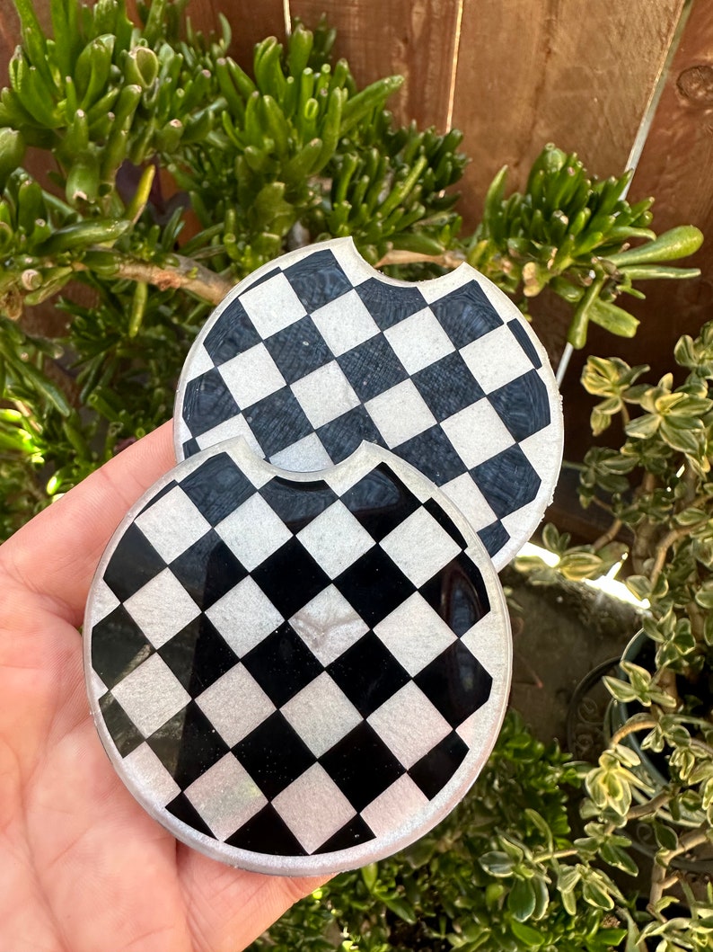 May include: Two black and white checkered round coasters with a glossy finish.