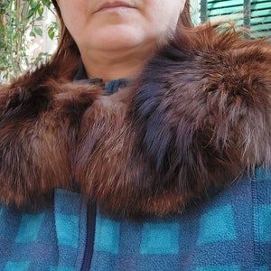 May include: A brown fur collar, likely fox or similar, worn over a blue and teal fleece jacket. The fur is a mix of dark and light brown tones, creating a textured appearance. The jacket has a plaid pattern.