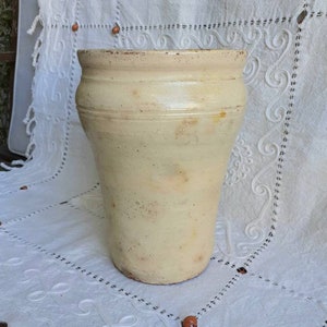 May include: A large, off-white ceramic vase with a rounded bottom and a slightly flared top. The vase has a rustic, aged appearance with subtle variations in colour and texture.