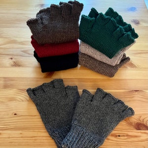 May include: Several stacks of fingerless gloves in various colors, including brown, red, black, green, tan, and gray. The gloves are knitted and have a scalloped edge. The gloves are displayed on a light wooden surface.