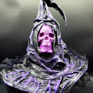 May include: A pointed hat featuring a purple skull face mask integrated into the front. The hat is constructed from black material with a textured, crinkled finish and vibrant purple highlights throughout the fabric and the skull mask.