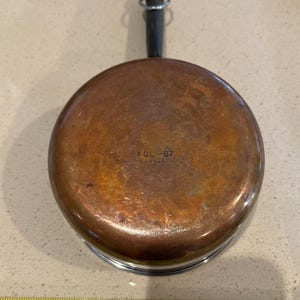 May include: Copper saucepan with a black handle and a blue and white rim. The bottom of the pan has the text "1 Qt - 87" stamped on it.