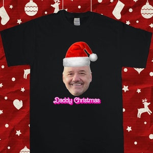 May include: Black t-shirt with a photo of a man wearing a Santa hat and the text "Daddy Christmas" in pink.