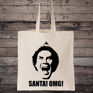 May include: A white canvas tote bag featuring a black silhouette of Buddy the Elf from the film Elf. The silhouette depicts Buddy with his mouth open in a surprised expression. The text "SANTA! OMG!" is printed in black below the silhouette.