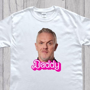 May include: White t-shirt with a photo of a man's face and the word "Daddy" in pink letters.