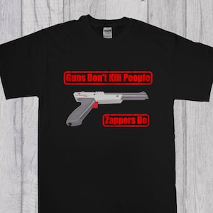 May include: Black t-shirt featuring a red graphic of a NES Zapper gun. The graphic reads "Guns Don't Kill People Zappers Do."
