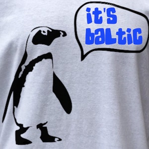 May include: A white t-shirt with a black silhouette of a penguin and a speech bubble that says "it's baltic".