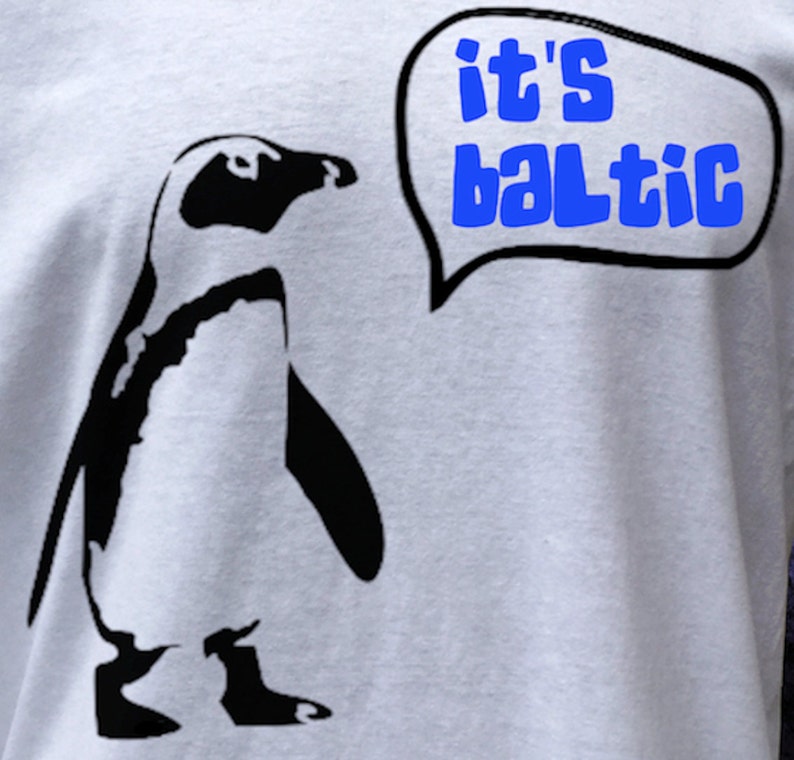 May include: A white t-shirt with a black silhouette of a penguin and a speech bubble that says "it's baltic".