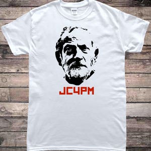 Peut inclure: T-shirt blanc avec une image en noir et blanc d'un visage d'homme et le texte "JC4PM" en rouge.