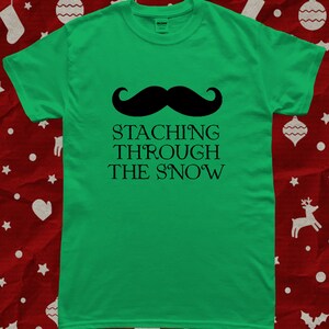 May include: Green t-shirt with a black mustache and the text "STACHING THROUGH THE SNOW".