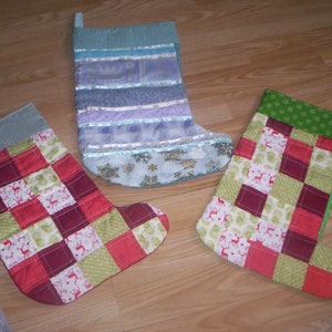 May include: Three Christmas stockings, one blue with white and silver trim, one red and green patchwork, and one green and white patchwork.