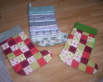 Op de afbeelding: Drie kerstsokken, één blauw met witte en zilveren versiering, één rood-groen patchwork en één groen-wit patchwork.