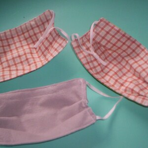 Peut inclure: Trois masques faciaux, deux avec un motif &agrave; carreaux rouge et blanc et un uni gris clair.