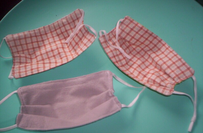 Peut inclure: Trois masques faciaux, deux avec un motif &agrave; carreaux rouge et blanc et un uni gris clair.
