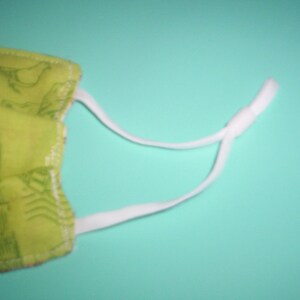 Peut inclure: Un masque facial en tissu vert avec un &eacute;lastique blanc. Le masque a un motif de petits motifs blancs.