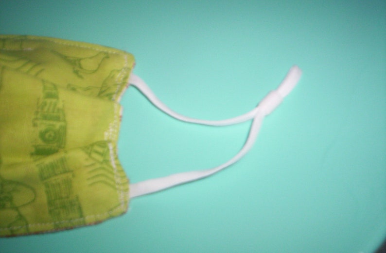 Peut inclure: Un masque facial en tissu vert avec un &eacute;lastique blanc. Le masque a un motif de petits motifs blancs.