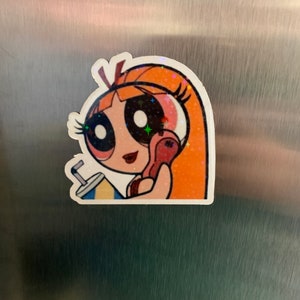 May include: A sticker of a cartoon girl with orange hair, wearing a pink shirt and holding a red phone. She has large eyes and a red lipstick. The sticker has a glittery finish.