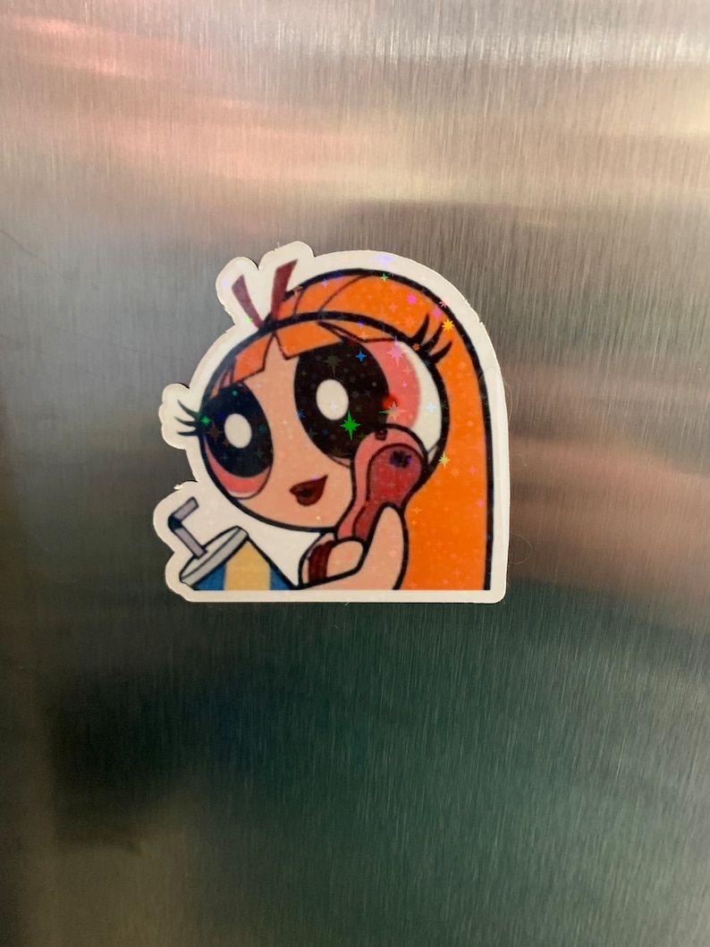 May include: A sticker of a cartoon girl with orange hair, wearing a pink shirt and holding a red phone. She has large eyes and a red lipstick. The sticker has a glittery finish.