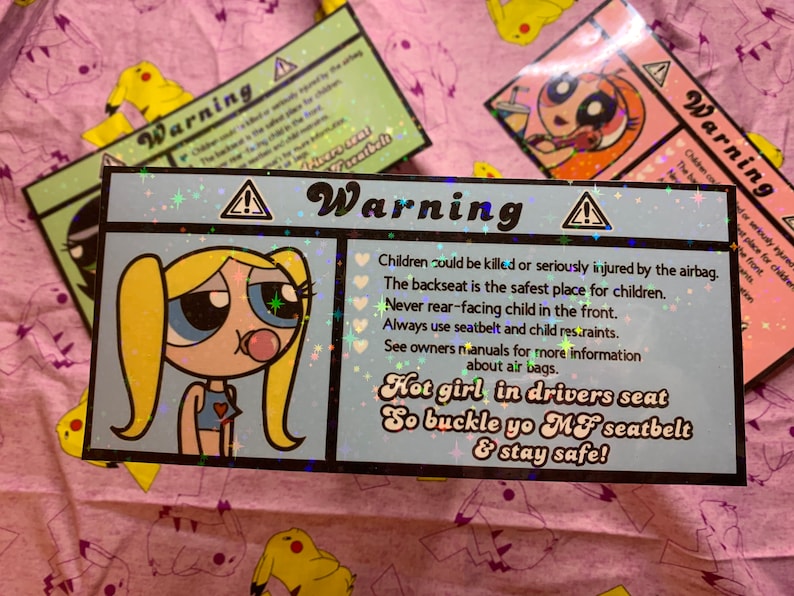May include: A blue and white warning sign with a cartoon girl with blonde pigtails and a pink bubble. The sign reads "Warning" and includes safety tips for children in cars. The text also says "Hot girl in drivers seat So buckle yo MF seatbelt & stay safe!"
