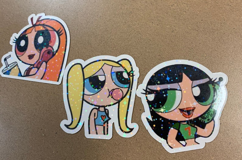 May include: Three cartoon character stickers with glitter accents. The characters are from the Powerpuff Girls cartoon. The first sticker is of Bubbles, the second is of Buttercup, and the third is of Blossom.