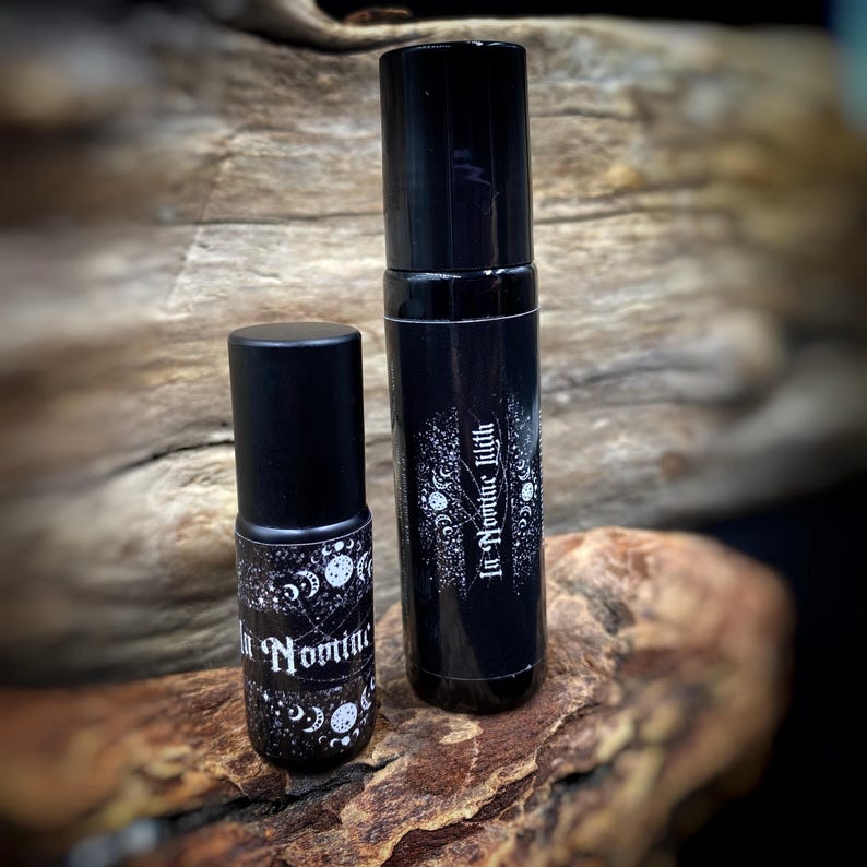 May include: Two black cylindrical bottles with matching black caps. The bottles have white text and celestial designs. The bottles are on a piece of wood.