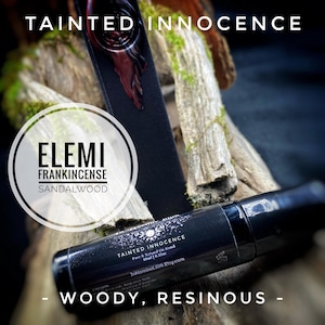 May include: A black essential oil roller bottle with the text "TAINTED INNOCENCE" and "ELEMI FRANKINCENSE SANDALWOOD." The bottle is 10ml / 0.33oz. The background features wood and moss, with the words "WOODY, RESINOUS."