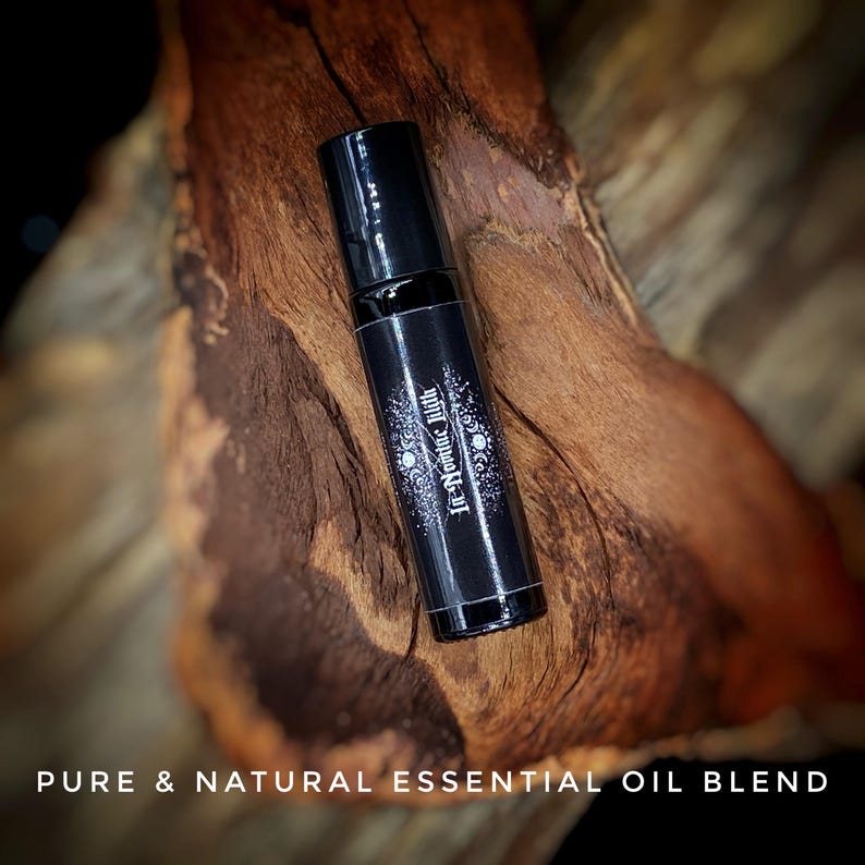 May include: A black essential oil roller bottle with the text "Ir-Yoniic Lilith" and a moon design. The bottle is set against a textured, brown wooden background. The words "PURE & NATURAL ESSENTIAL OIL BLEND" are at the bottom.