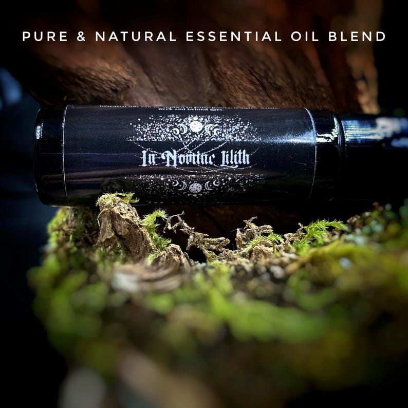 May include: A black essential oil blend bottle with the text "In Nomine Lilith" and "Pure & Natural Essential Oil Blend". The bottle is set on a bed of green moss and wood.