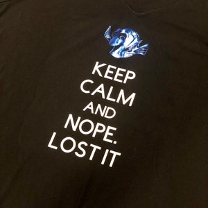 May include: Black t-shirt with a white graphic that says "Keep Calm and Nope. Lost It."  A blue and white cartoon fish is above the text.
