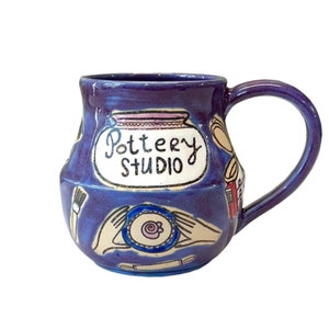 May include: Purple ceramic mug with a white label that says "Pottery Studio" and illustrations of pottery tools and supplies.