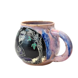 May include: A handmade ceramic mug with a unique design. The mug features a black background with a white illustration of a person meditating under a tree. The mug has a purple, blue, and pink glaze and a large handle.