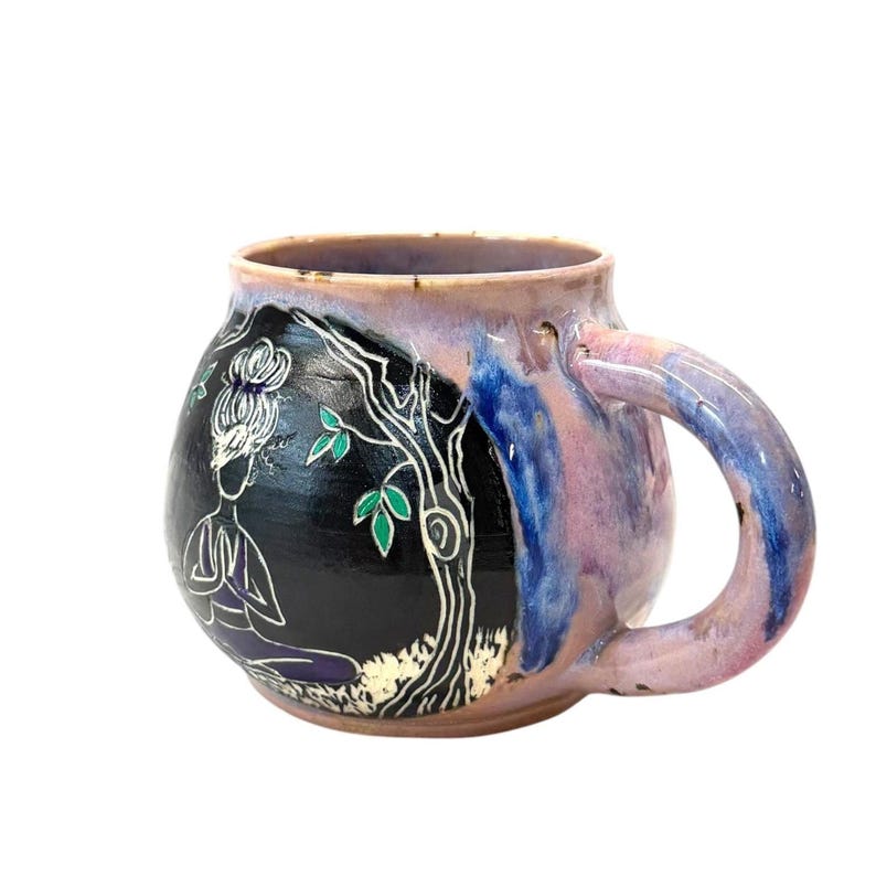 May include: A handmade ceramic mug with a unique design. The mug features a black background with a white illustration of a person meditating under a tree. The mug has a purple, blue, and pink glaze and a large handle.