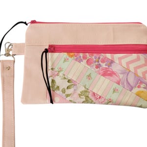 May include: A pink fabric pouch with a floral print and a pink zipper. The pouch has a pink strap with a silver clasp.