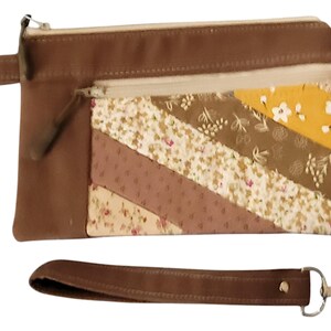 May include: A brown fabric zippered pouch with a patchwork design featuring floral and geometric patterns in shades of brown, yellow, and white. The pouch has a detachable brown strap with a silver hook.