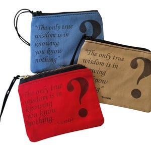 Op de afbeelding: Drie kleine ritszakjes met een vraagtekenontwerp en de quote "De enige ware wijsheid is te weten dat je niets weet." van Socrates erop gedrukt. De zakjes zijn rood, blauw en bruin.