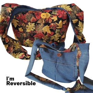 May include: Reversible shoulder bag with a fall leaf pattern on one side and denim on the other. The leaf pattern features red, orange, and yellow leaves on a black background. The denim side has a pocket and a wooden button closure.