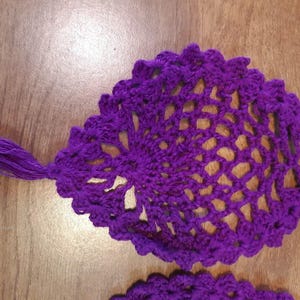May include: Purple crocheted doily with a tassel. The doily has a delicate, lacy design.