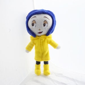 May include: A handmade doll of a character with a light grey face, blue hair, and a yellow coat. The doll has a smiling expression and is wearing black trousers and yellow wellington boots. The doll is against a white background.