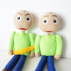 May include: Two plush dolls with tan heads, embroidered facial features, green shirts, blue pants, and brown feet. One doll has a yellow ruler around its waist. The dolls are handmade.