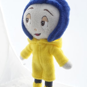Puede incluir: Mu&ntilde;eca de peluche de un personaje con rostro blanco, ojos bordados y una peque&ntilde;a sonrisa. La mu&ntilde;eca viste una capucha azul y un impermeable amarillo con botas a juego. Los brazos de la mu&ntilde;eca est&aacute;n extendidos, sobre un fondo blanco.