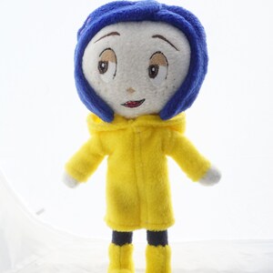 Puede incluir: Mu&ntilde;eca de peluche hecha a mano de un personaje con rostro blanco, ojos bordados y boca roja. La mu&ntilde;eca lleva una peluca azul, un impermeable amarillo con capucha y botas amarillas.