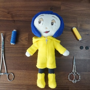 Puede incluir: Una mu&ntilde;eca de peluche hecha a mano con cabello azul y un abrigo amarillo, que se asemeja a un personaje. Suministros de costura, incluyendo tijeras, hilo y botones, est&aacute;n dispuestos alrededor de la mu&ntilde;eca sobre una superficie de madera. La mu&ntilde;eca mide aproximadamente 20 cm de altura.