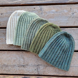 Peut inclure: Cinq bonnets en tricot dans un dégradé de couleurs, du blanc au vert au bleu. Les bonnets sont disposés en demi-cercle, le bonnet blanc en haut et le bonnet bleu en bas.