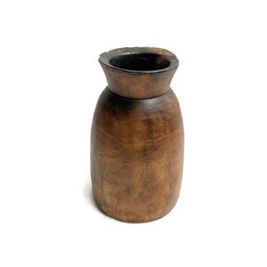 Op de afbeelding: Een donkerbruine houten vaas met een rond lichaam en een licht uitlopende bovenkant.
